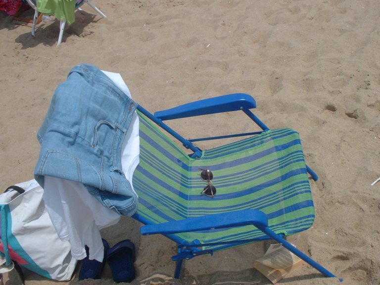 A folding beach chair, sandals, and bags on Ocean City sand